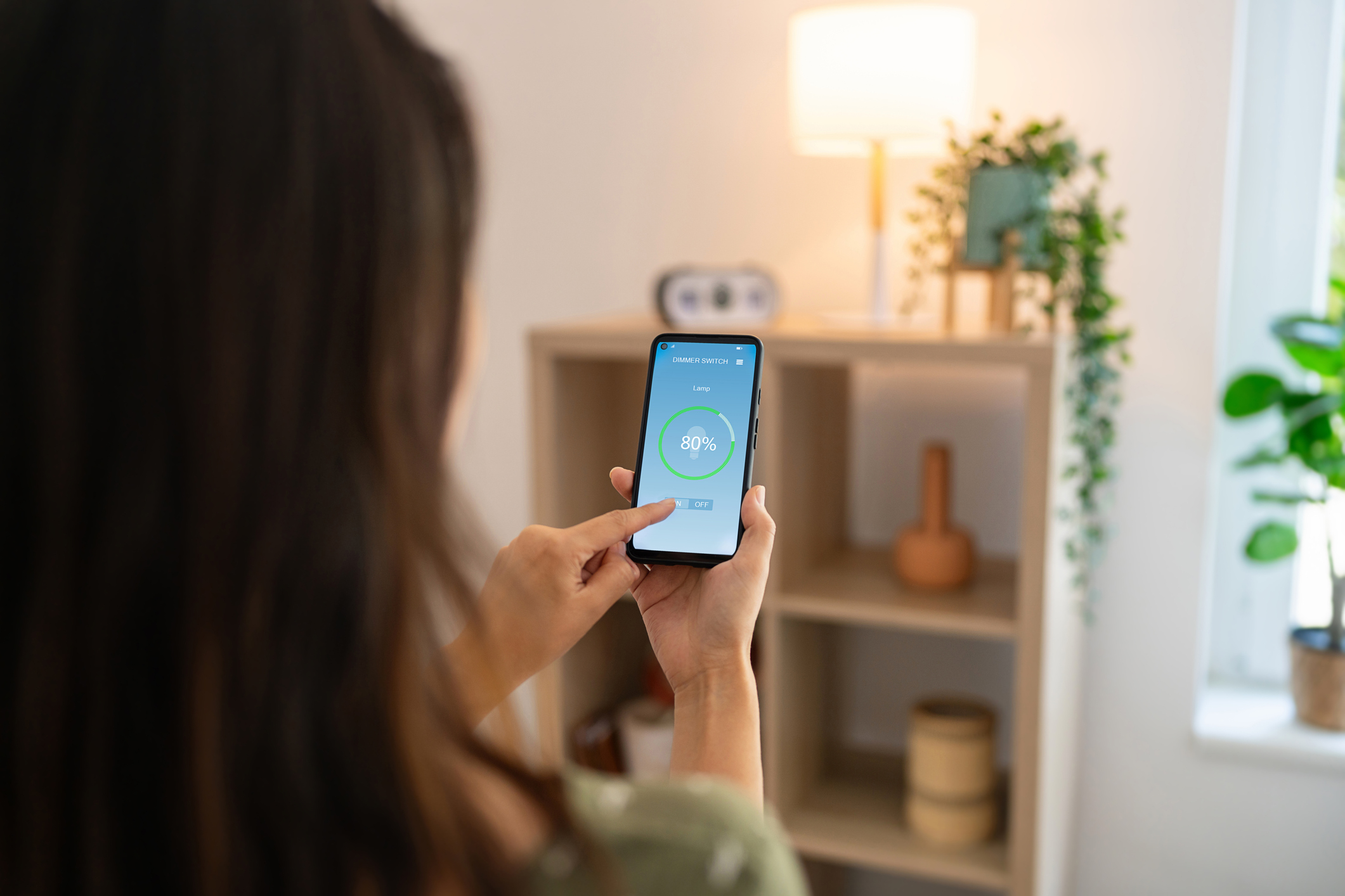 Woman controlling light with a smart phone at home.